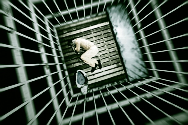 Man Lying Down In Fetal Position In Jail Cell
